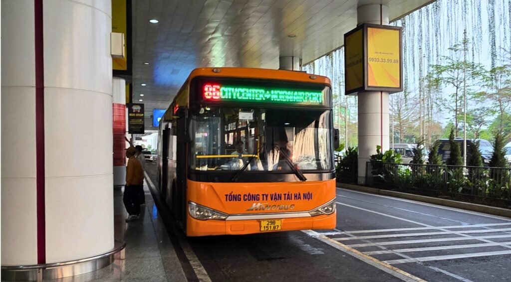 Bus 86 naranja en la terminal del aeropuerto de Hanoi con el cartel LED "86 City Center - Noi Bai Airport"