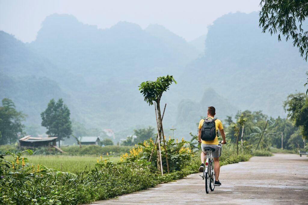 Ciclista paseando en bicicleta por un camino rural entre arrozales y montañas en Vietnam