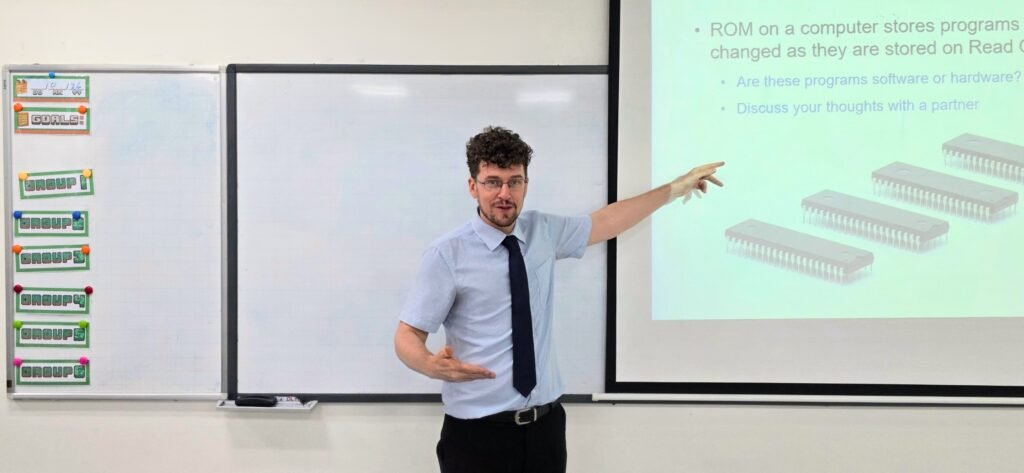 Alberto dando clase de informática señalando una diapositiva sobre ROM y software en un colegio de Hanoi