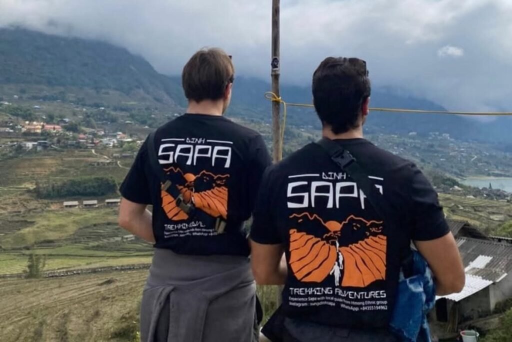 Dos viajeros de espaldas con la camiseta de Dinh Sapa Trekking Adventures mirando el valle de Sapa