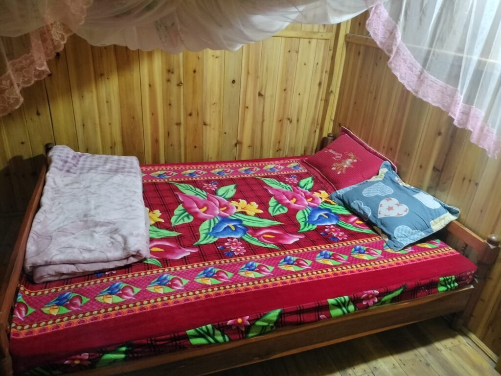 Cama con mosquitera y colcha de flores en una habitación de madera en casa de Mama Vu Vi, Sapa