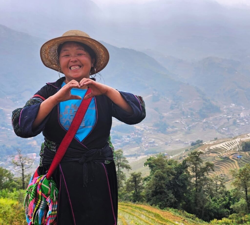Mama Vu Vi haciendo un gesto de corazón con las manos, con el valle y los arrozales de Sapa al fondo