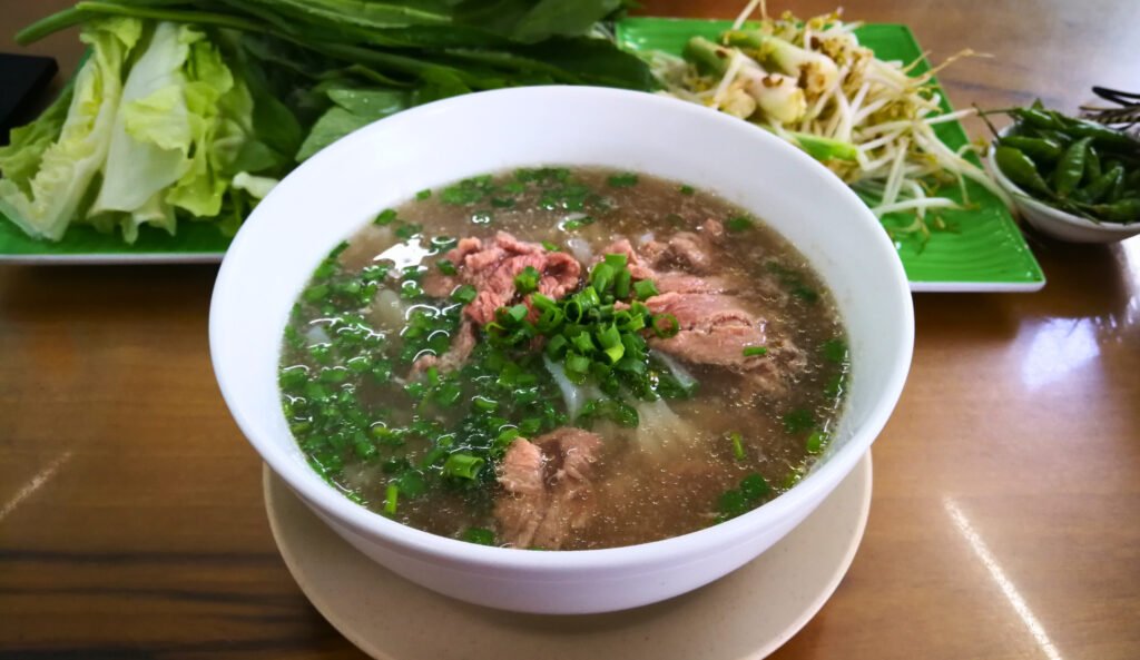 Bol de phở bò vietnamita con ternera, cebolleta y guarnición de hierbas y brotes
