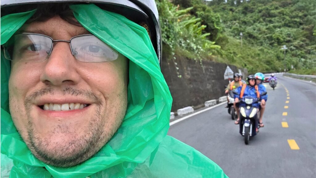 Alberto con chubasquero verde y casco recorriendo el Hai Van Pass en moto bajo la lluvia, con otros miembros del tour detrás en la carretera