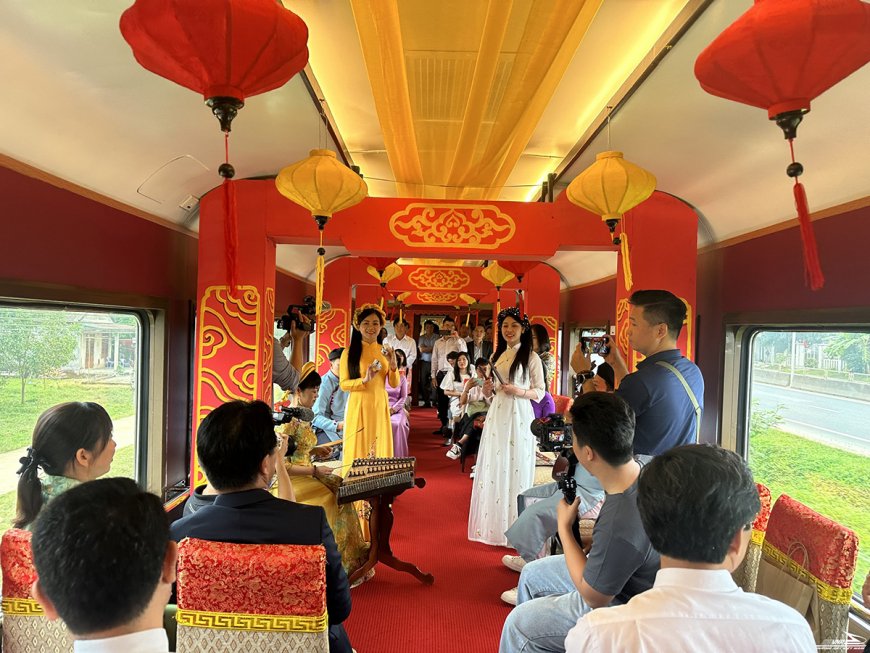 Interior del tren turístico del Hai Van Pass decorado con farolillos rojos y amarillos, con músicos tocando instrumentos tradicionales vietnamitas ante los pasajeros (asientos VIP).